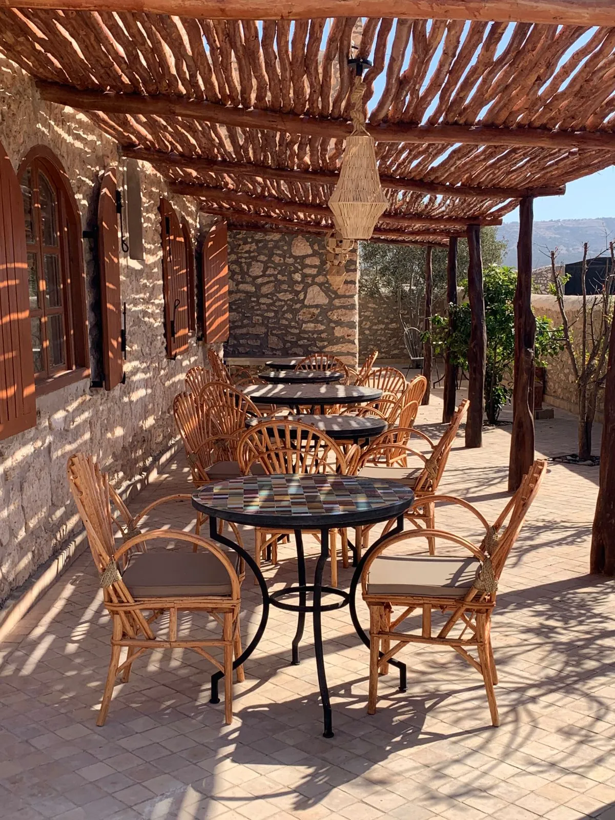 Terrasse ensoleillée de la maison d'hôtes Villa'S à Essaouira avec tables en mosaïque et chaises en rotin sous une pergola en bois