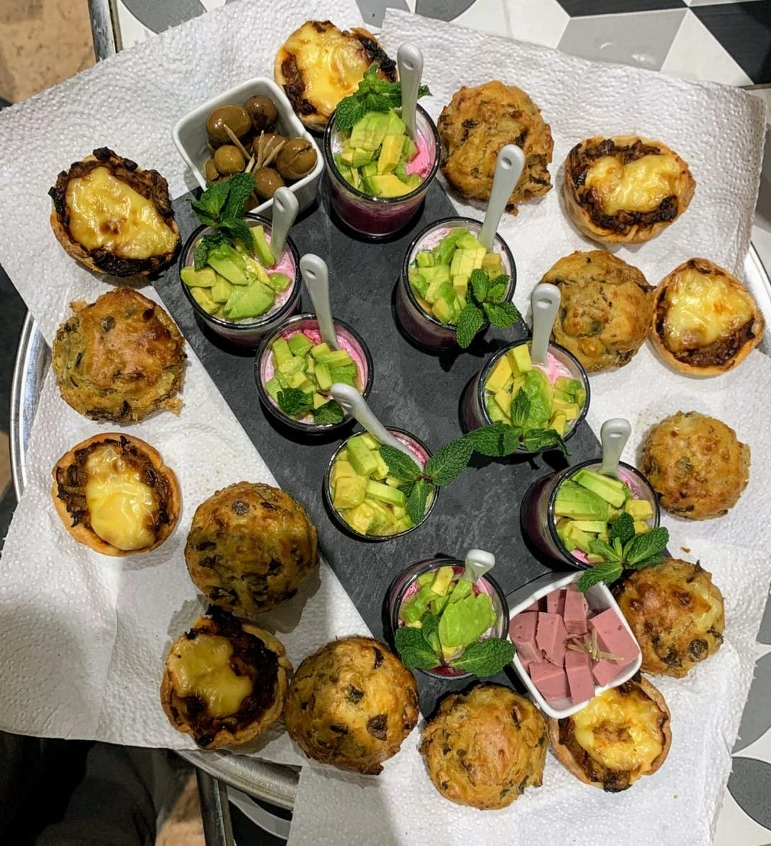 Plateau d'amuse-bouches avec muffins salés, mini quiches au fromage, verrines d'avocat et betterave, olives et dés de charcuterie.